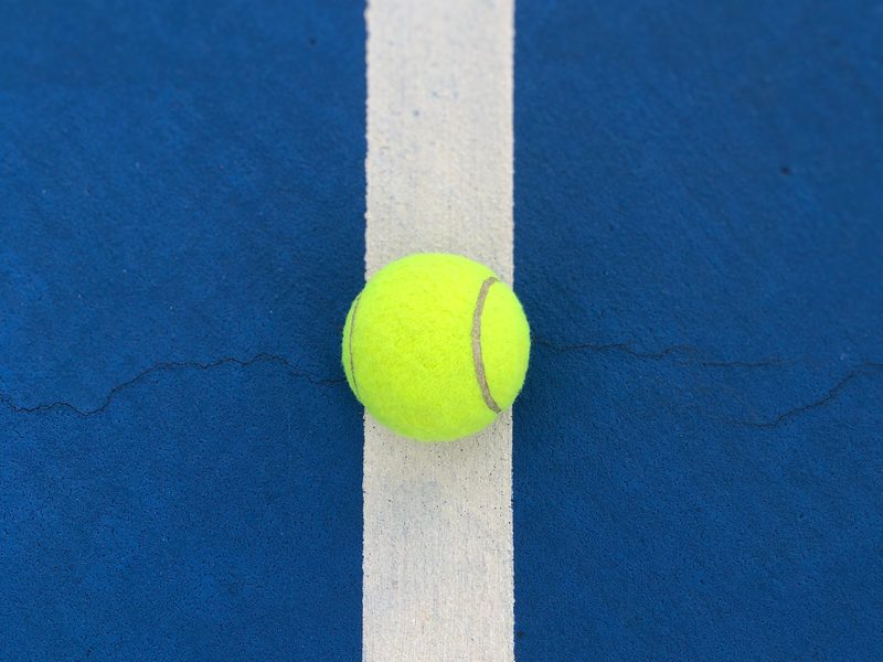 A tennis ball on a white line on a blue court