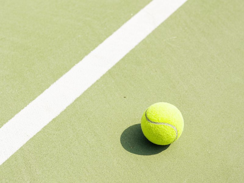 A tennis ball beside a white line on a green court