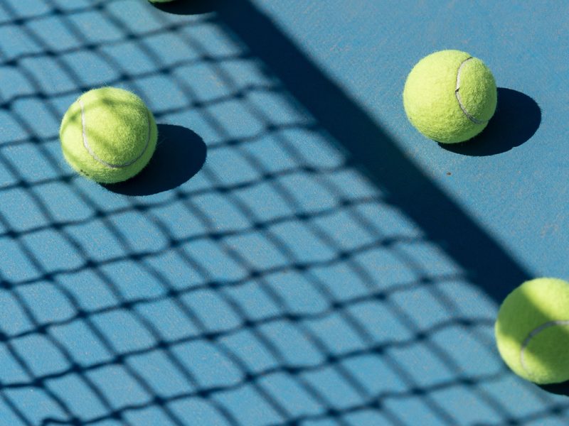 Tennis balls on a blue court under the shadow of the net