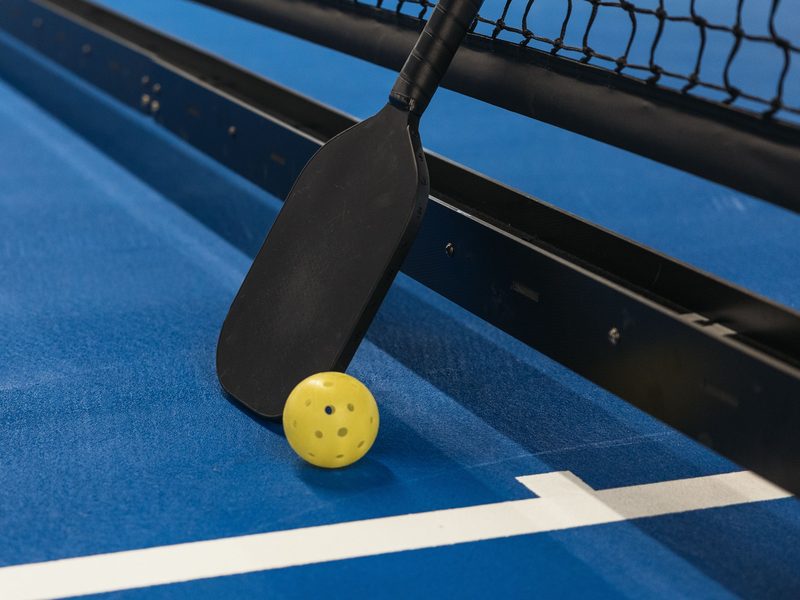 A pickleball paddle and ball resting against a net on a blue court