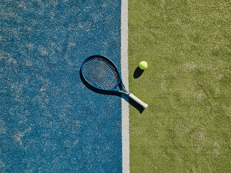 A tennis racket and ball on a blue and green court