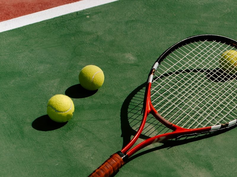 A red tennis racket and three balls on a green court
