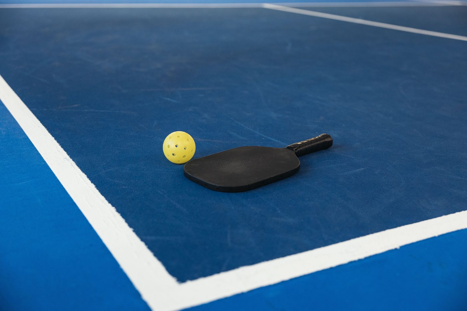 A pickleball paddle and yellow ball on a blue court