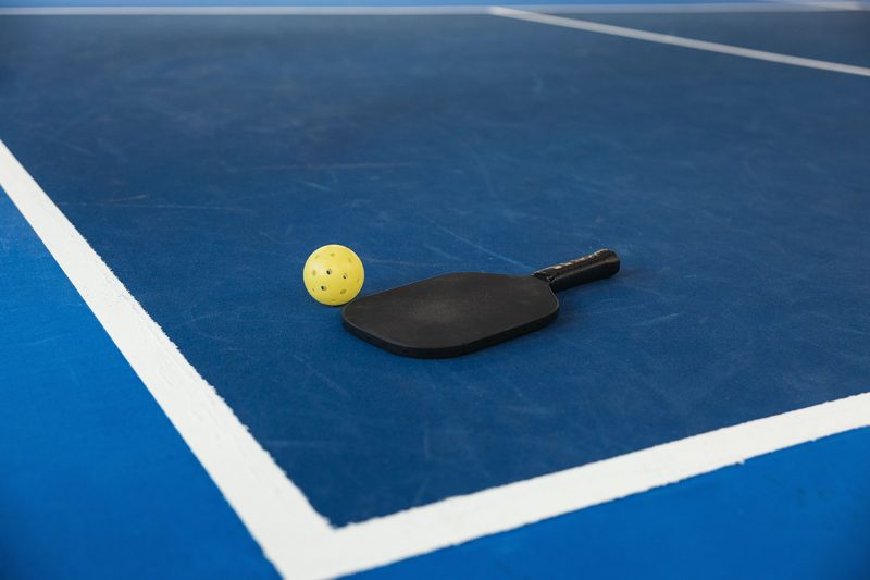 A pickleball paddle and yellow ball on a blue court